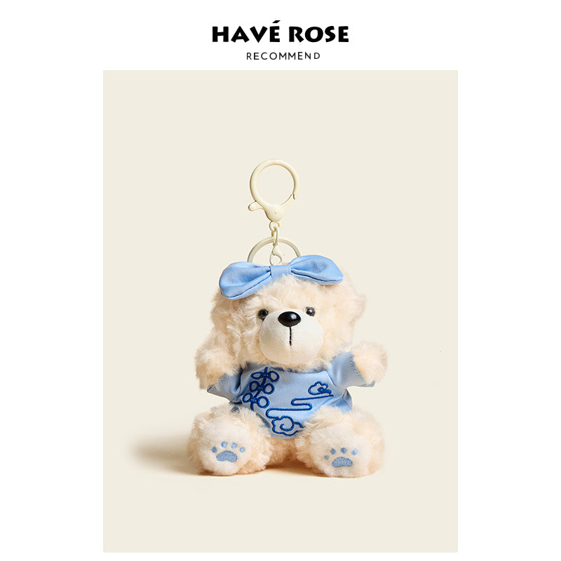 Teddy bear keychain with blue dress and bow on a beige background, branded 'Hçôve Rose'.