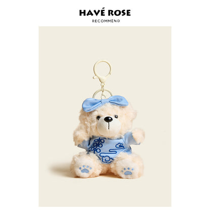 Teddy bear keychain with blue dress and bow on a beige background, branded 'Hçôve Rose'.