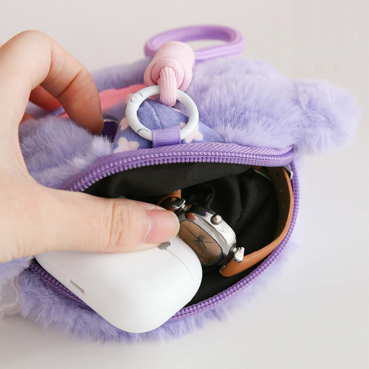 Purple fluffy pouch with a hand holding an AirPods case and keychain.