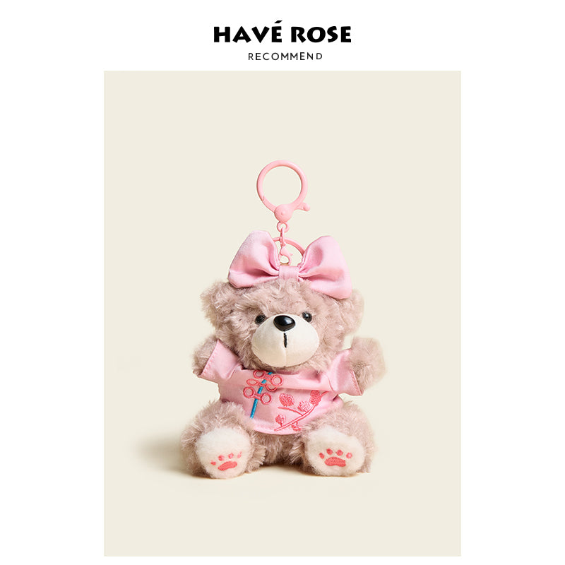 Plush teddy bear keychain with pink bow and dress on a beige background, featuring the brand 'Have Rose'.