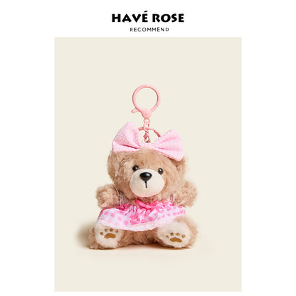 Teddy bear keychain with pink bow and dress on a beige background, featuring the brand 'Hçáve Rose'.