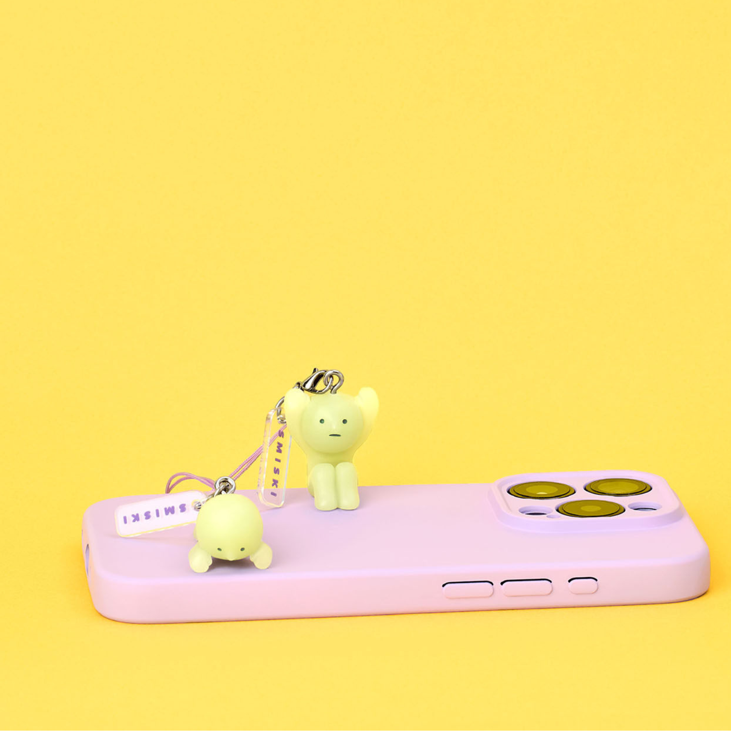 One SMISKI is lying on the phone, another one is sitting on it. SMISKI can be used as a phone chain