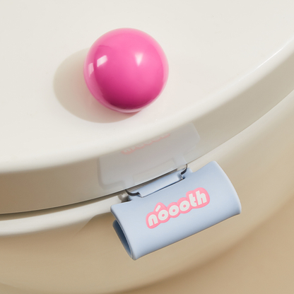 Pink ball on a toilet seat with a blue clip labeled 'néooth' Label Toilet Lifter